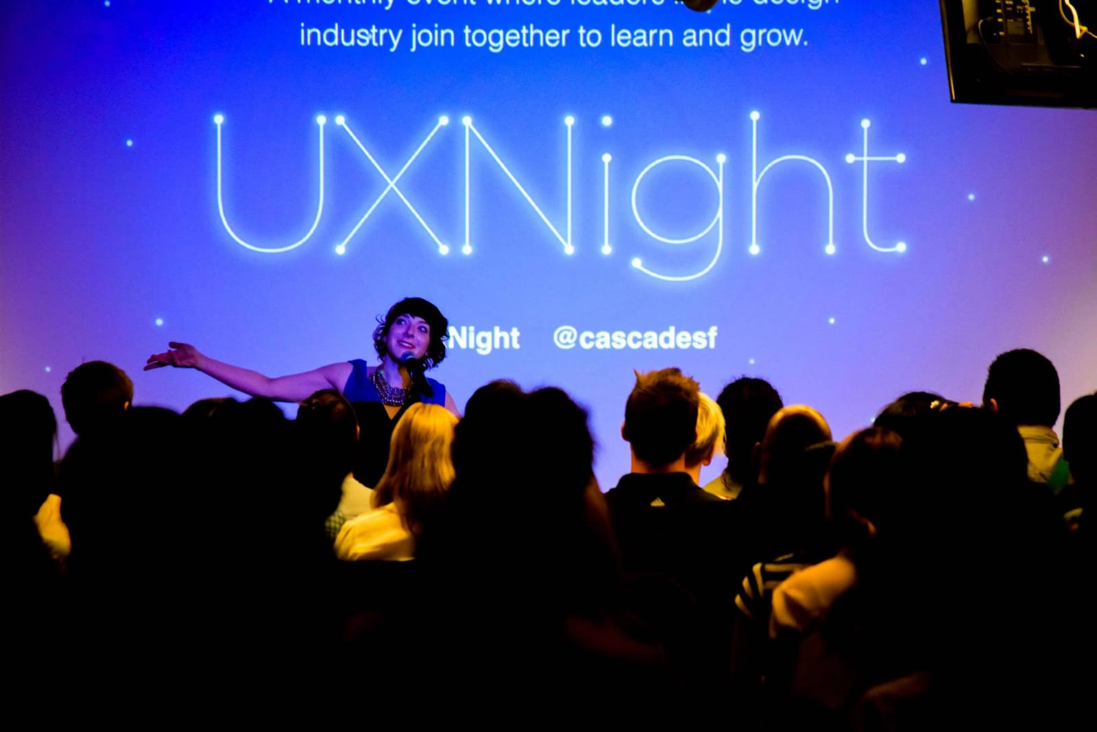 Andi Galpern speaking on stage at UXNight, a Cascade SF event, in front of a packed crowd