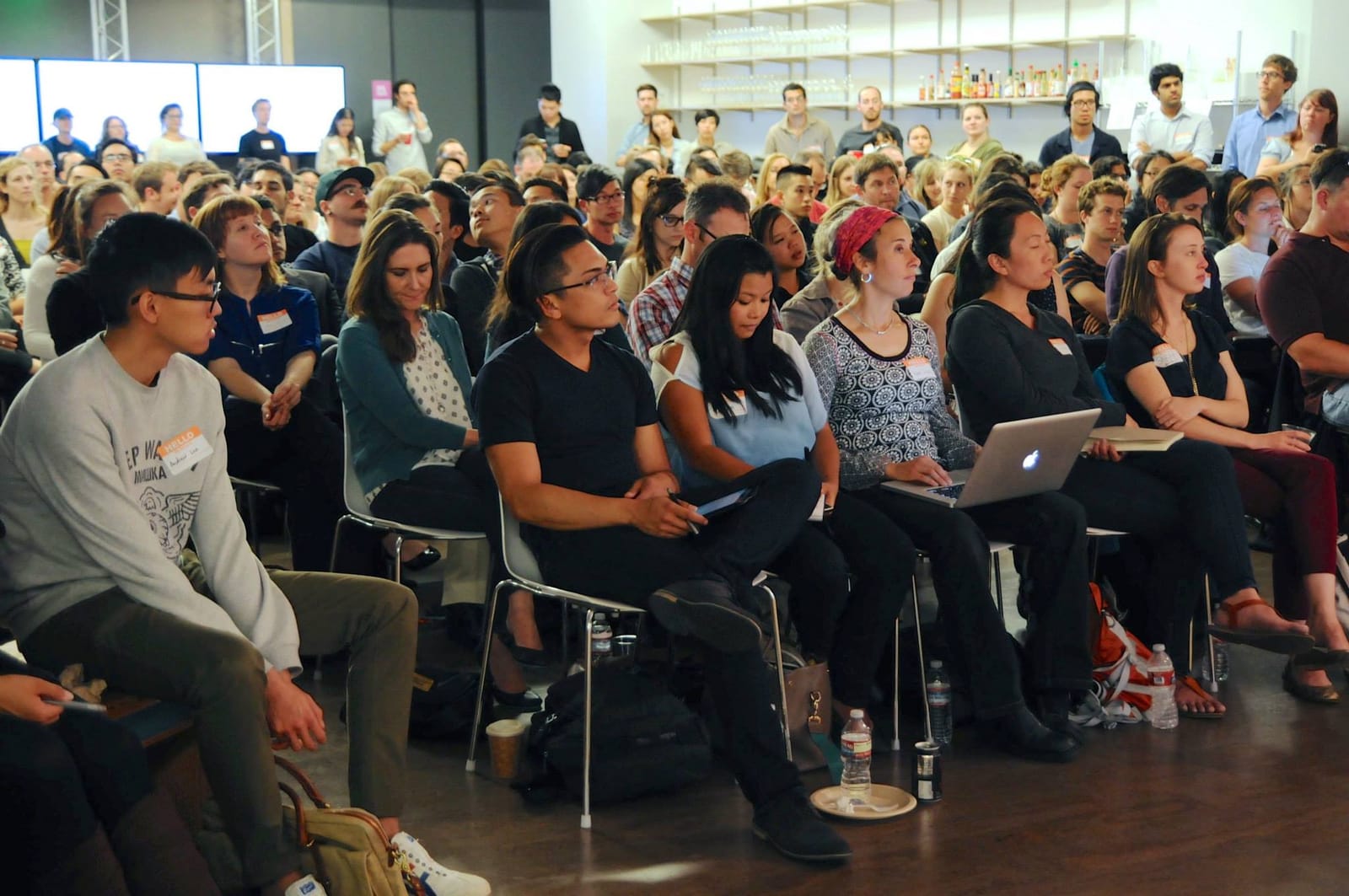 A packed, attentive audience wearing name tags seated in rows at a Cascade SF event in a modern loft space