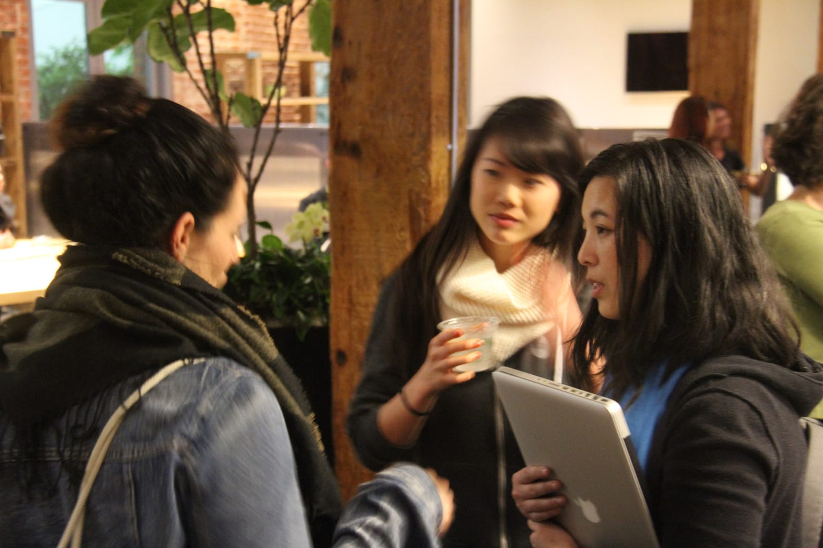 Three attendees in conversation at an event in a brick-and-beam venue