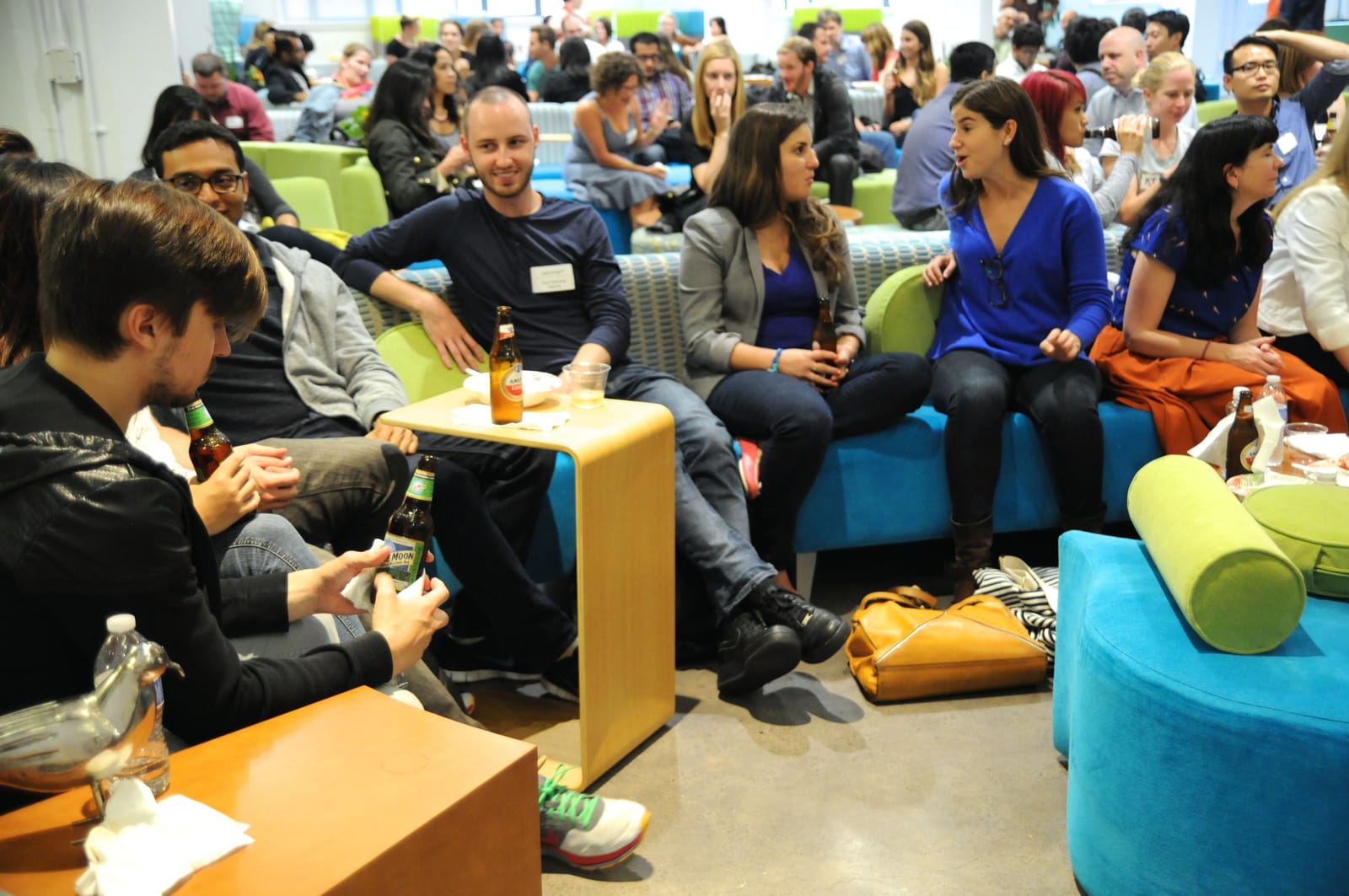 Attendees networking on colorful couches with drinks at a packed reception