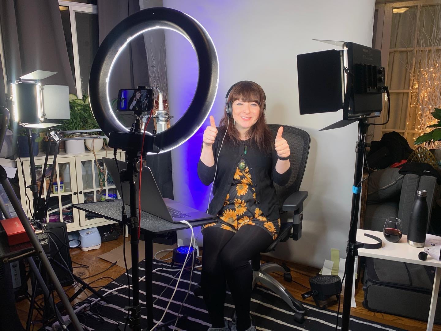 Andi Galpern giving two thumbs up at her home broadcast studio with a ring light, video lights, mic, and laptop